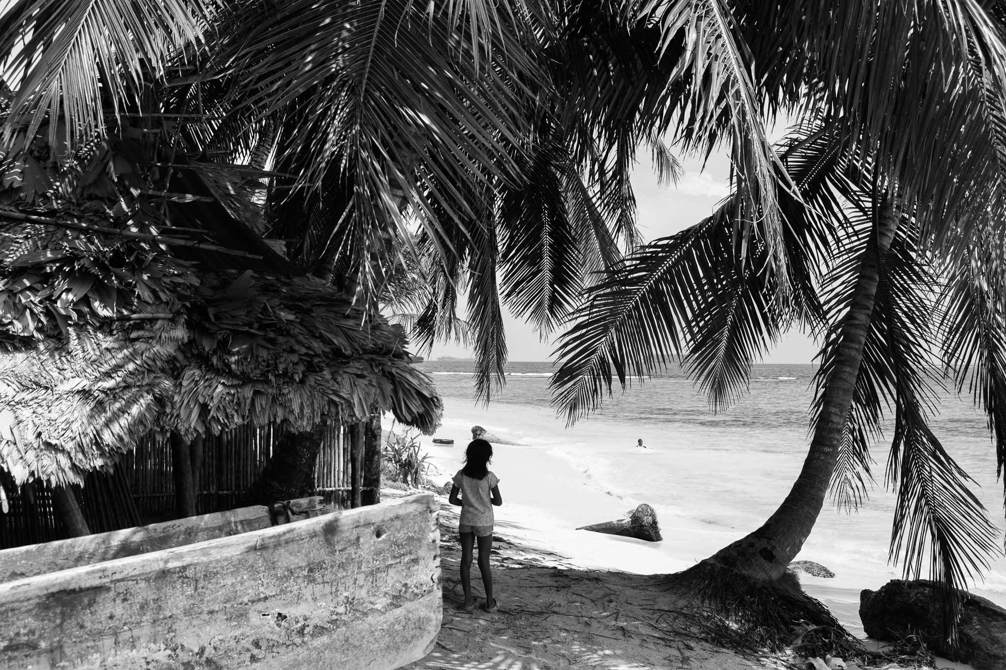 Niña bajo las palmeras mirando hacia la playa