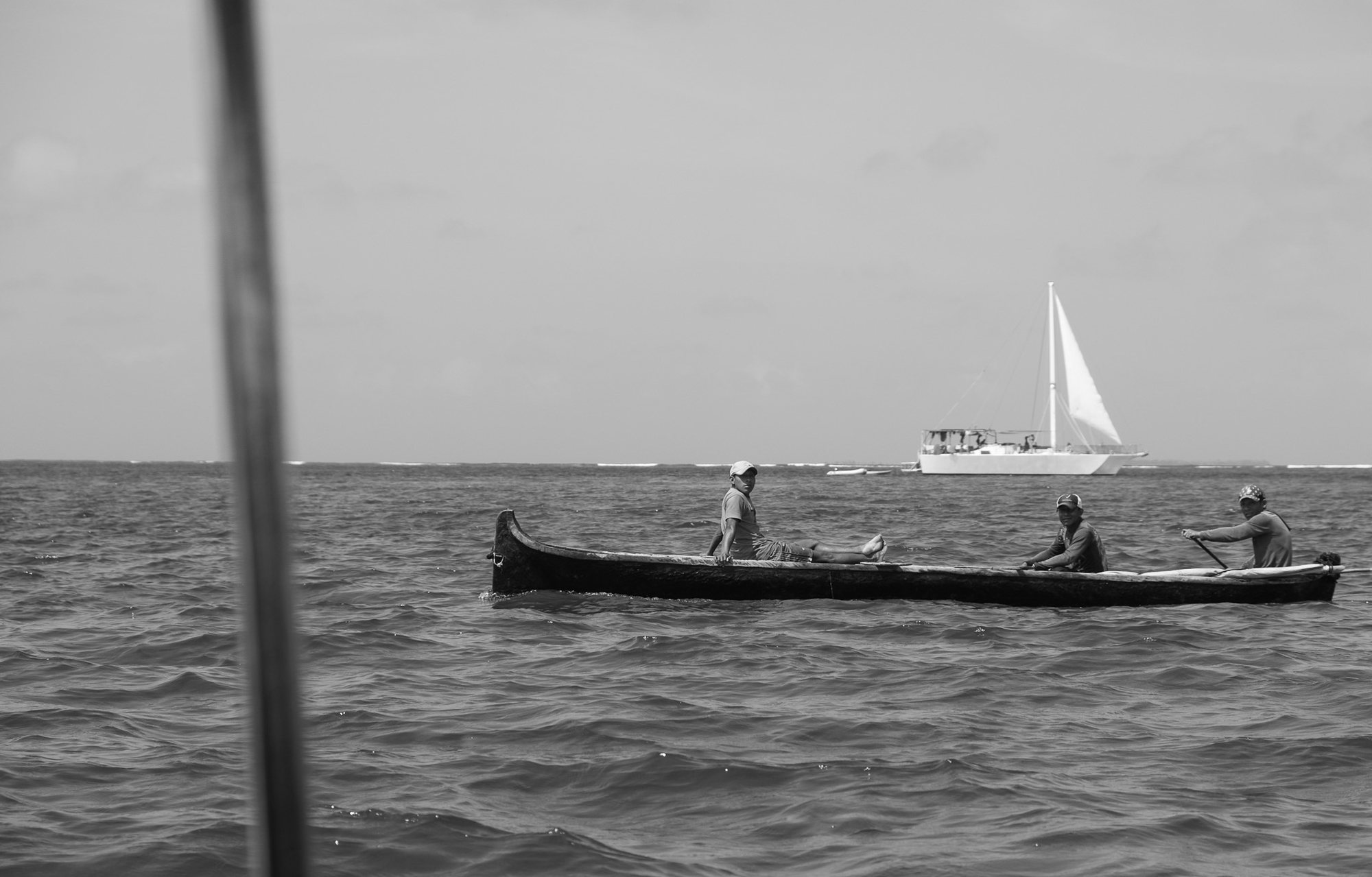 Cayuco con tres pescadores guna y un velero al fondo