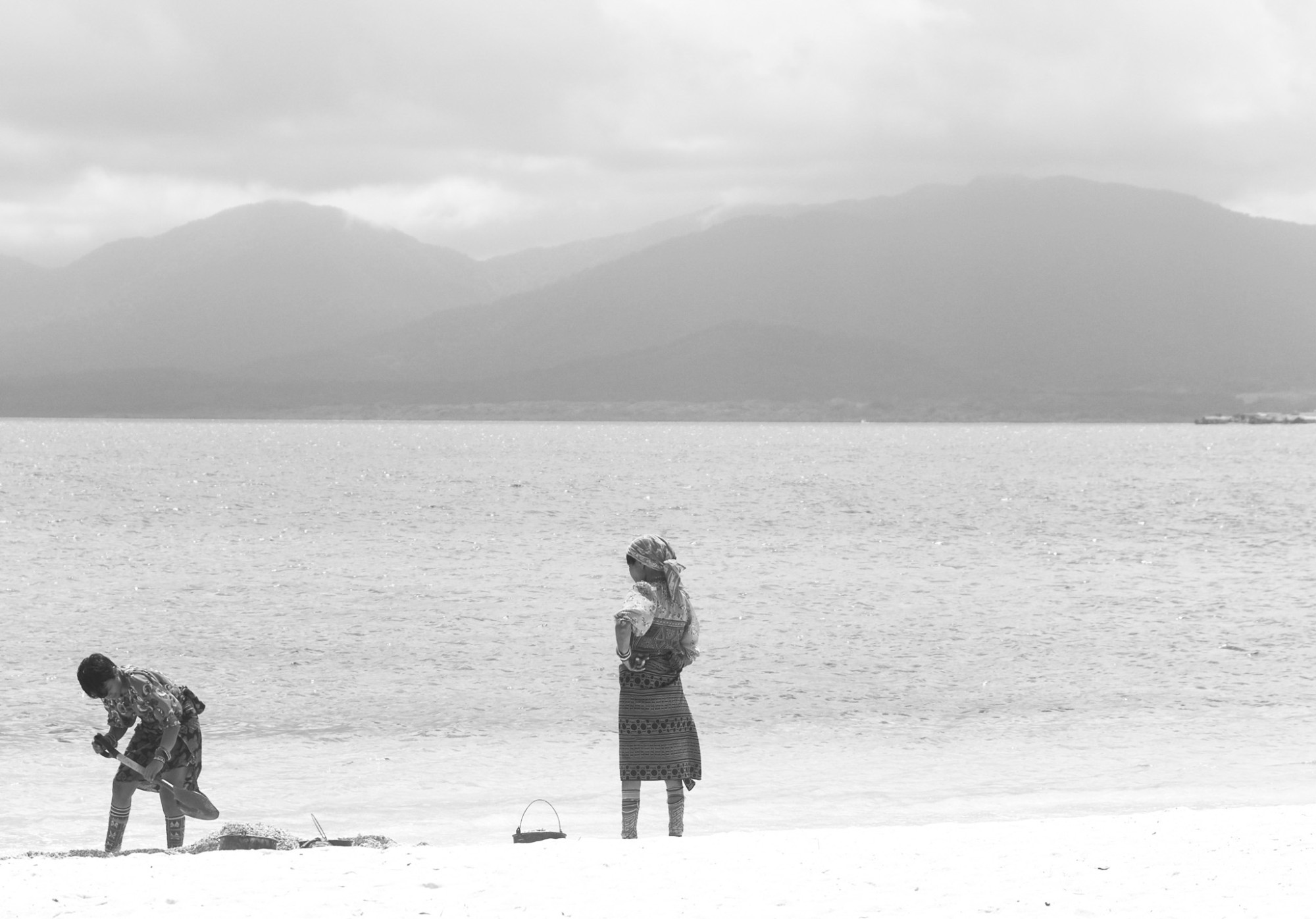 Dos mujeres guna en la playa frente al mar, con montañas al fondo